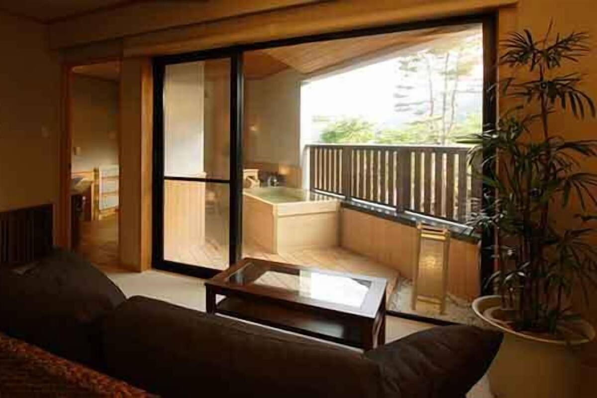 Un salon moderne avec un canapé, une table basse et une porte-fenêtre coulissante donnant sur un balcon d’où l’on peut admirer un immeuble et une piscine.