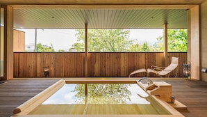 A wooden deck with a hot tub, two wicker chairs, and a view of trees and buildings. - Hotel Hakuba Hifumi (Hakuba)
