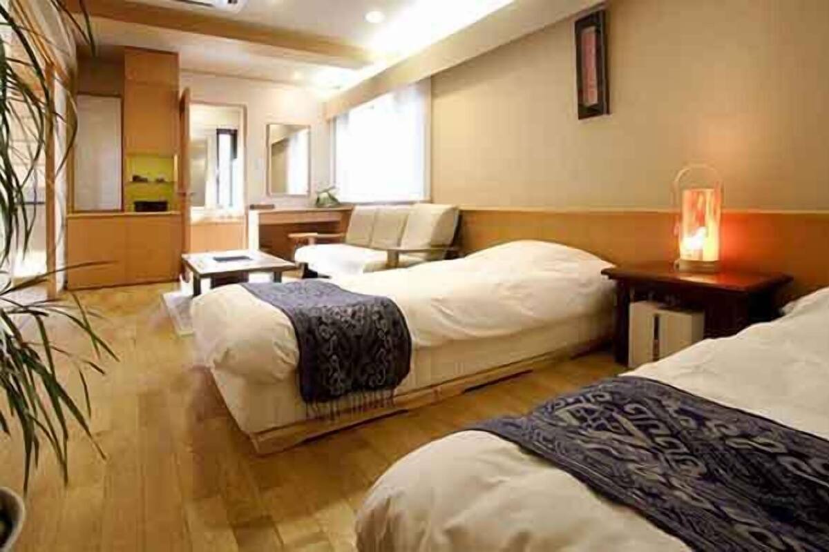 Une chambre d’hôtel avec deux lits, un bureau, une chaise, une petite table et une lampe de chevet.