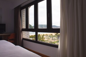 Habitación de hotel con una ventana grande, una cama, un escritorio con silla y un televisor.