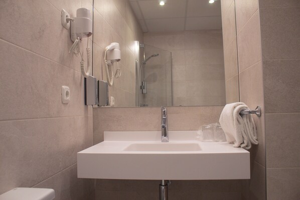 Un baño moderno con un lavamanos blanco, un secador de pelo de mano montado en la pared y una cabina de ducha de vidrio.