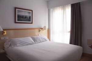 Una habitación de hotel con una cama grande, un cuadro enmarcado en la pared, dos lámparas de noche y una ventana con cortinas.