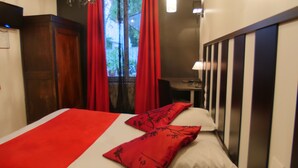 A hotel room with a bed, red curtains, a desk, and a window. - Hôtel Savary (La Rochelle)
