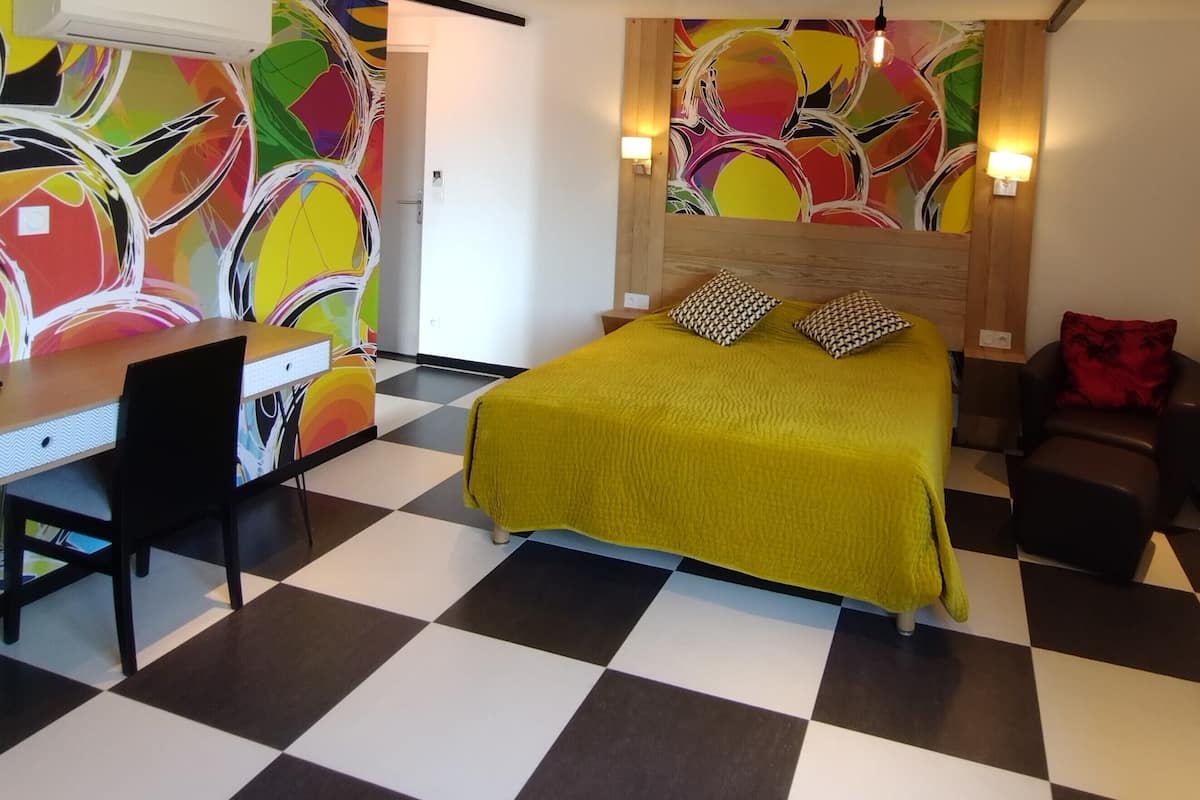 A room with a bed, a desk, a chair, a couch, and a colorful abstract wall.