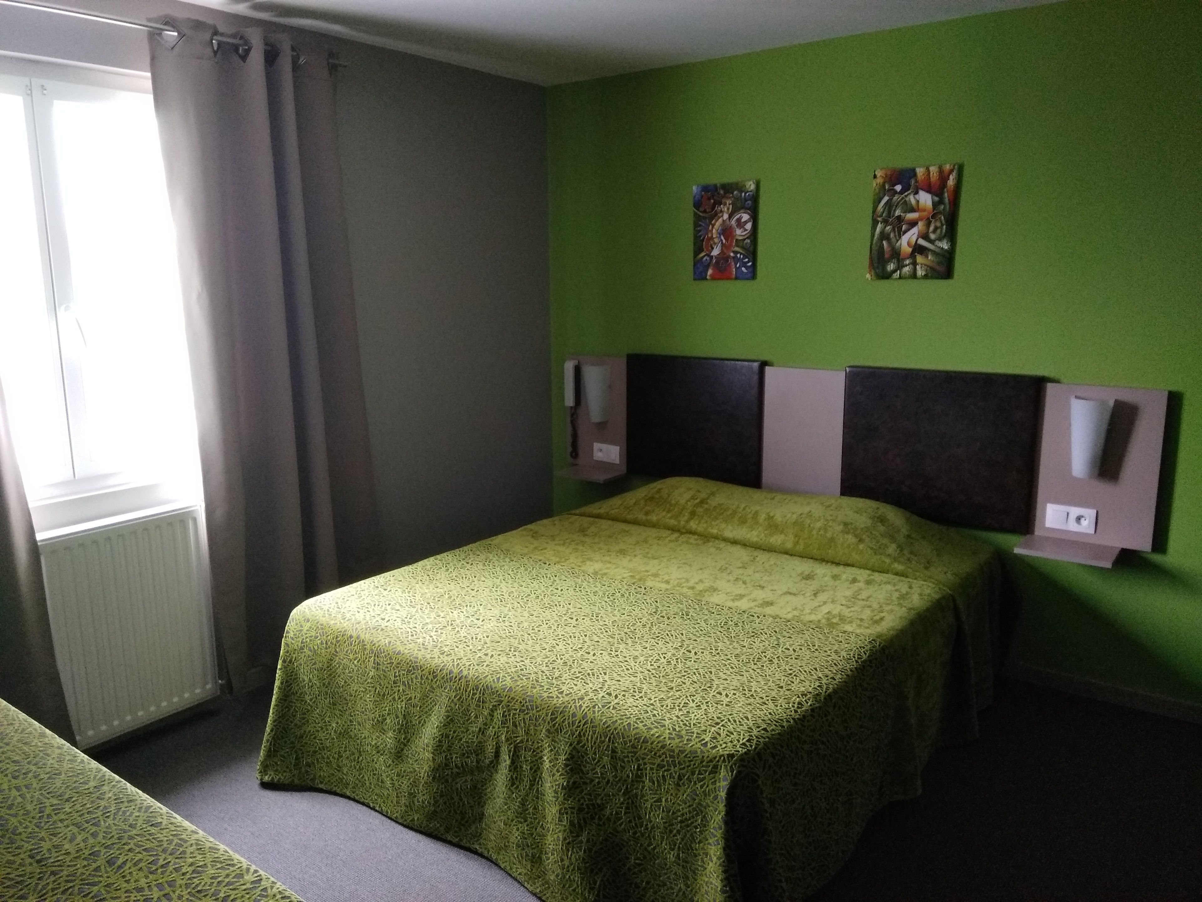 Une pièce avec un lit, une fenêtre avec des rideaux et deux tableaux accrochés au mur.