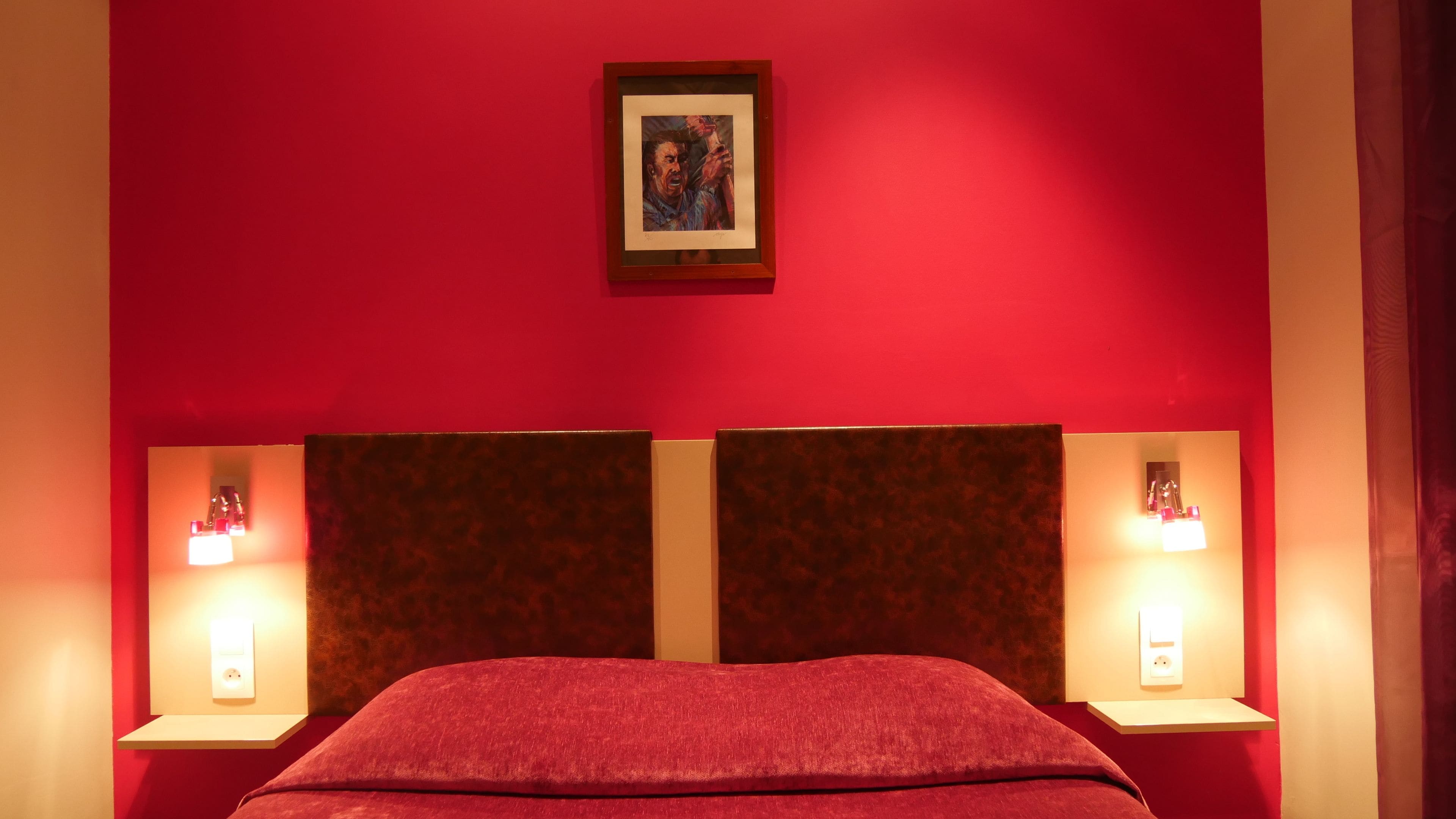 A room with a red wall, a framed picture above the bed, and two bedside lamps.