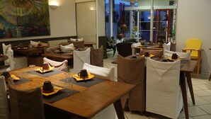 A restaurant with multiple tables set for dining, chairs with white covers, and a large abstract painting on the wall. - Hôtel Savary (La Rochelle)