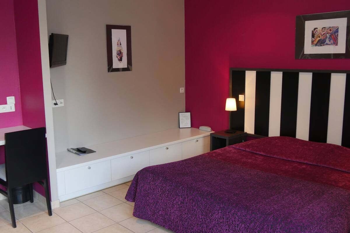 A bedroom with a bed, a desk, a chair, a nightstand, and a lamp.