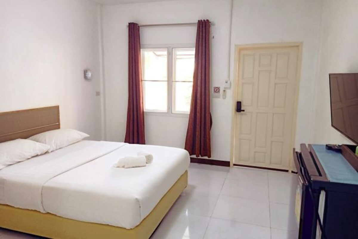 A hotel room with a bed, a television, a door, and curtains.