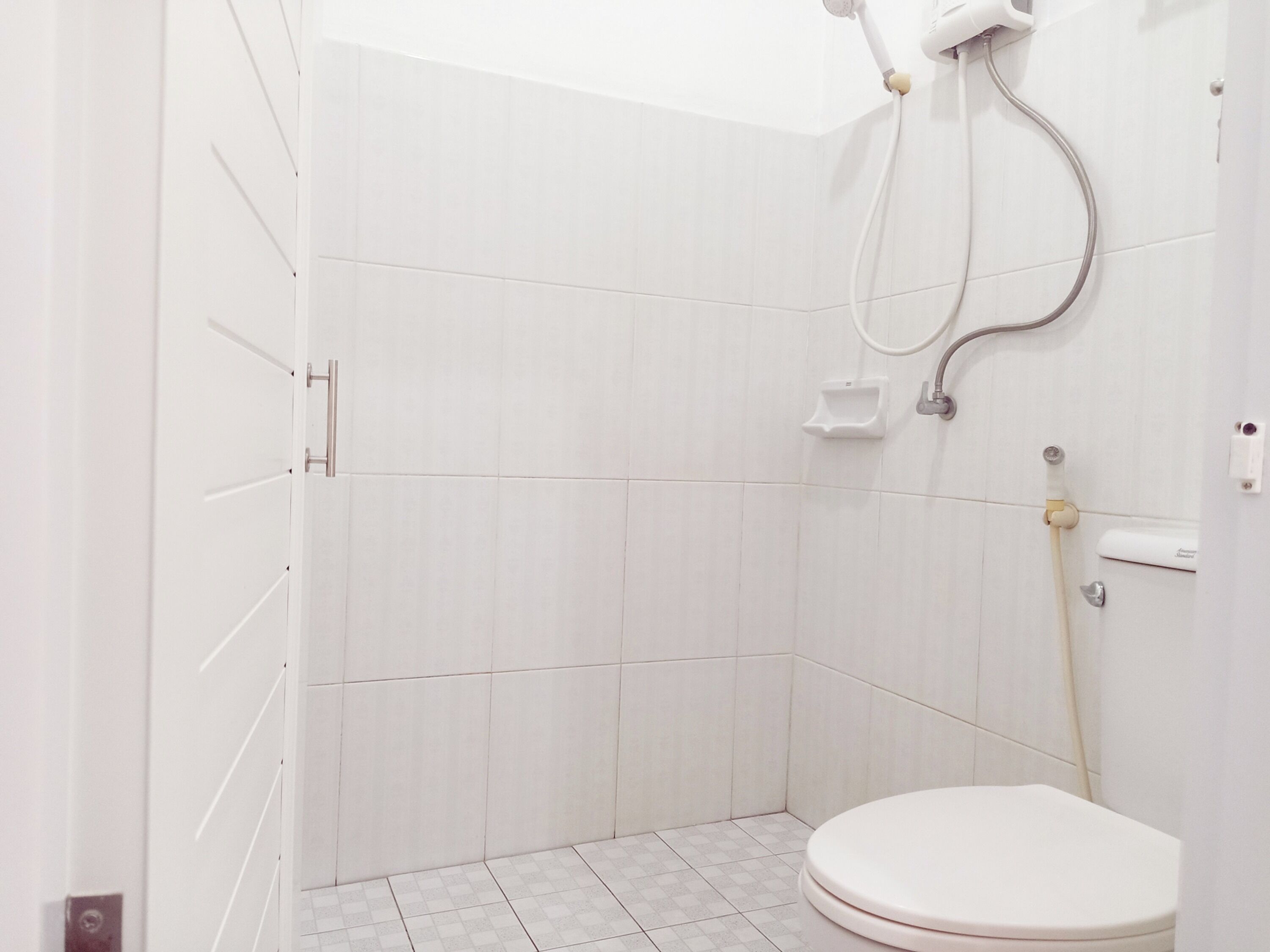 A small, white bathroom with a shower, toilet, and a hand dryer.