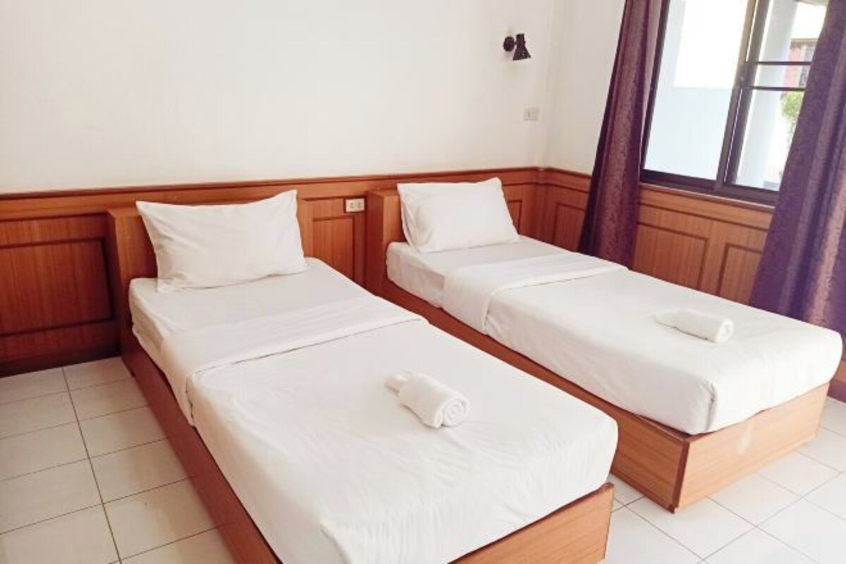 A hotel room with two single beds, wooden headboards, white bedding, and a window with curtains.