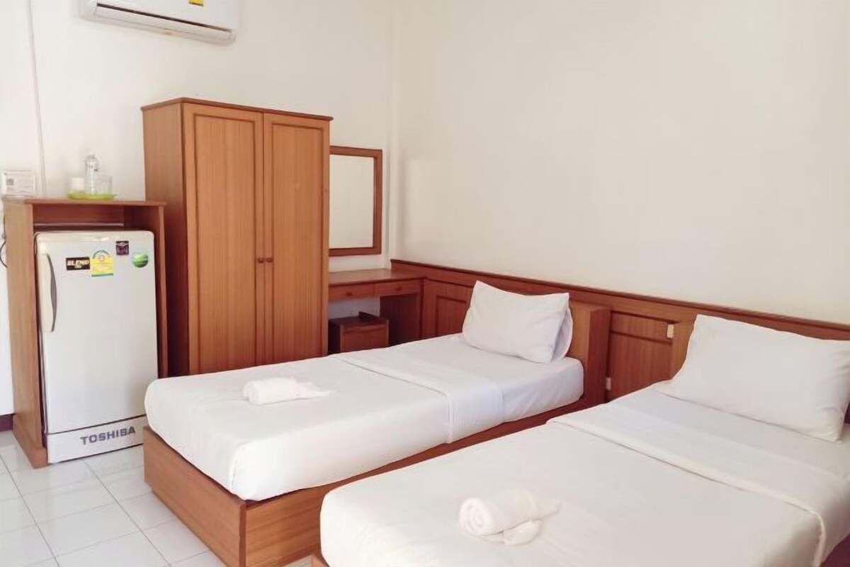 A hotel room with two single beds, a wooden wardrobe, a desk, and a refrigerator.