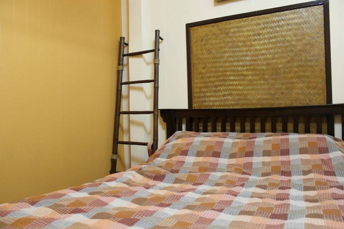 A bed with a checkered bedspread, a wooden headboard, and a bamboo ladder leaning against the wall.