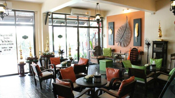 A cozy cafe with wooden furniture, green cushions, and a large leaf artwork on the wall.