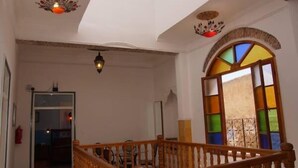 A spacious interior with a wooden staircase, a large arched window with colorful stained glass, and a ceiling with decorative light fixtures. - Riad Ksar El Jadida (El Jadida)