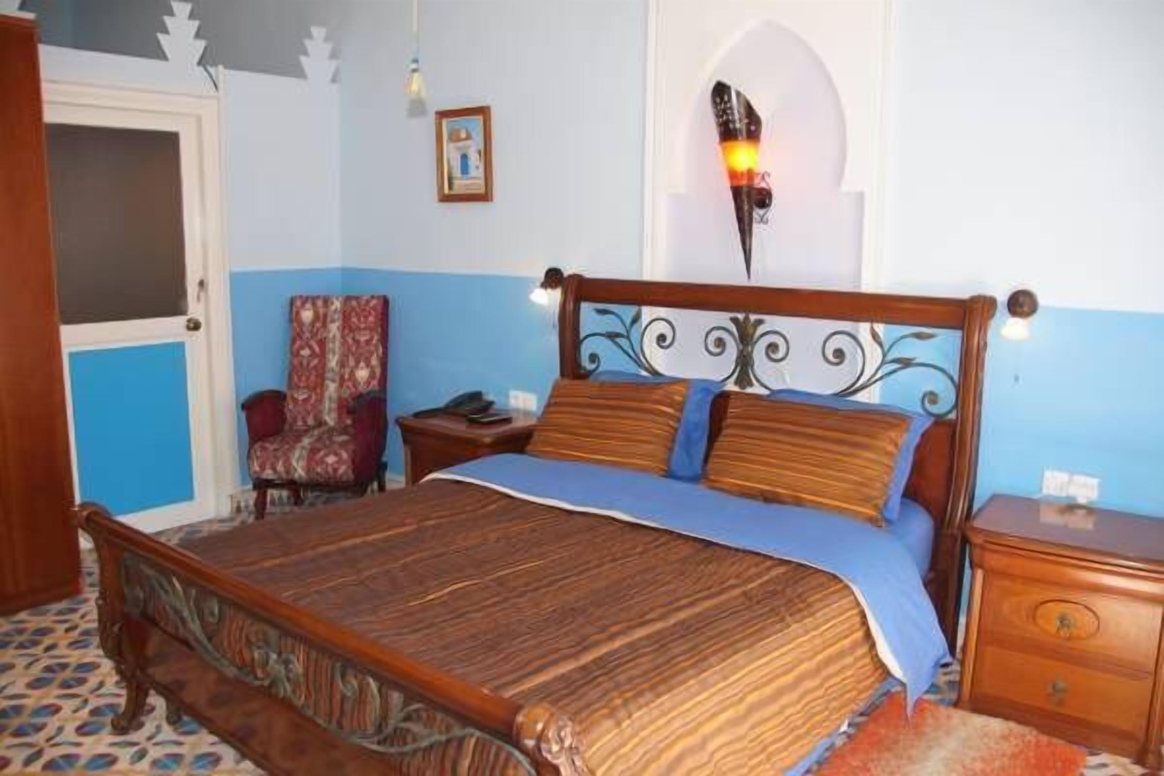 A bedroom with a wooden bed, a nightstand, a chair, and a wall-mounted lamp.