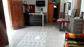 A spacious living area with a tiled floor, a wooden door, a black and white counter, and a patterned rug.