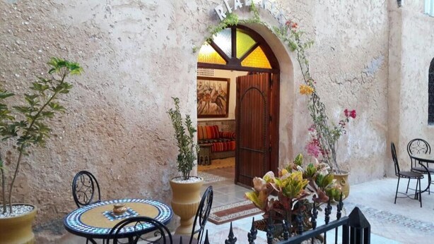 An interior courtyard with a rustic stone wall, a wooden door leading to a room with a red sofa, and potted plants. - Riad Ksar El Jadida (El Jadida)