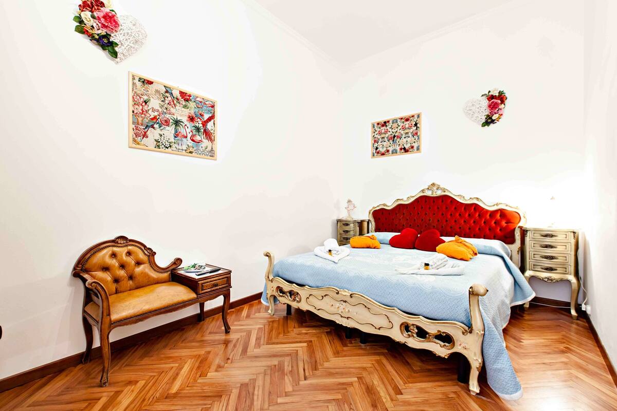 Un dormitorio con una cama, un banco de madera y dos adornos florales colgados en la pared.