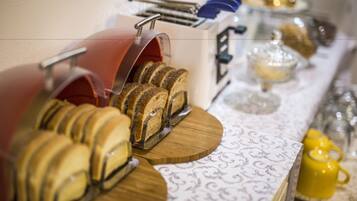 Ein Frühstücksbuffet mit verschiedenen Brotsorten und Gebäck, einer Kaffeemaschine und einem gelben Teekessel.