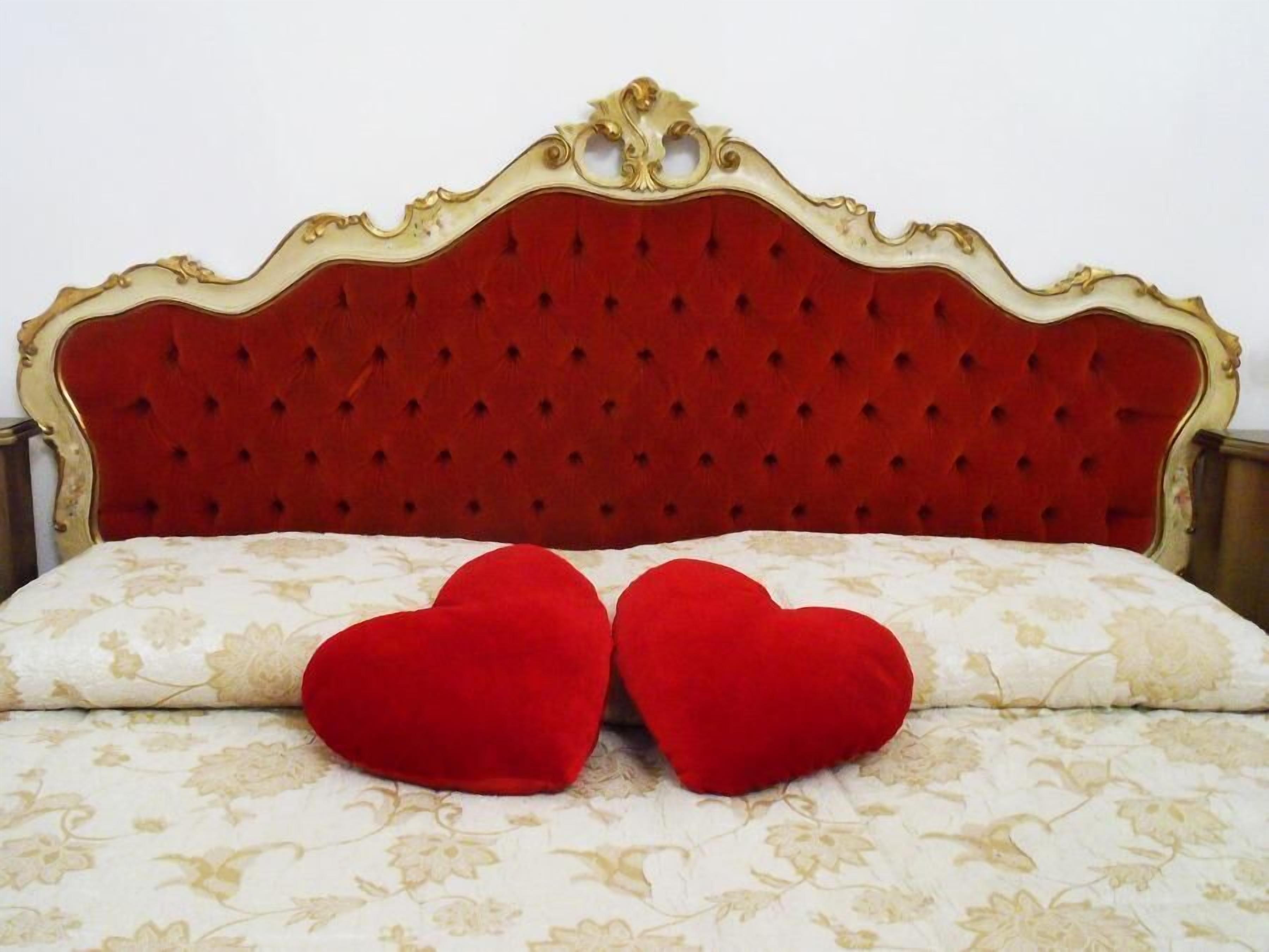 Una cama con cabecera tapizada en rojo y dos almohadas con forma de corazón rojo.