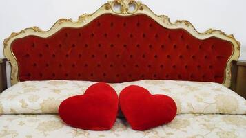 Una cama con cabecera tapizada en rojo y dos almohadas con forma de corazón rojo.
