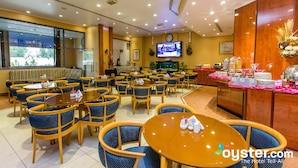 Een restaurantgedeelte in een hotel met ronde tafels en blauwe stoelen, een televisiescherm en een buffet.