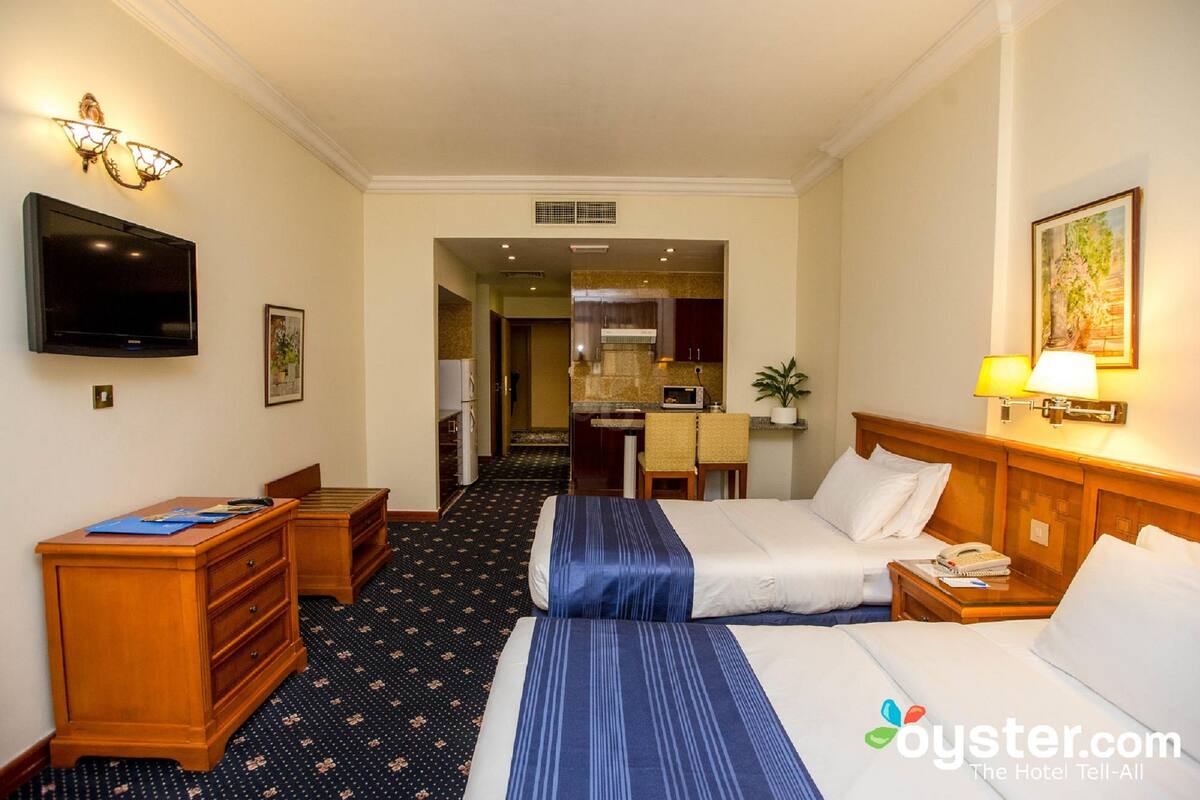 Een hotelkamer met twee bedden, een bureau, een televisie en een kitchenette op de achtergrond.