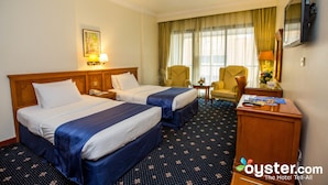 Een hotelkamer met twee bedden, een bureau, een stoel, een televisie en een raam met gordijnen.