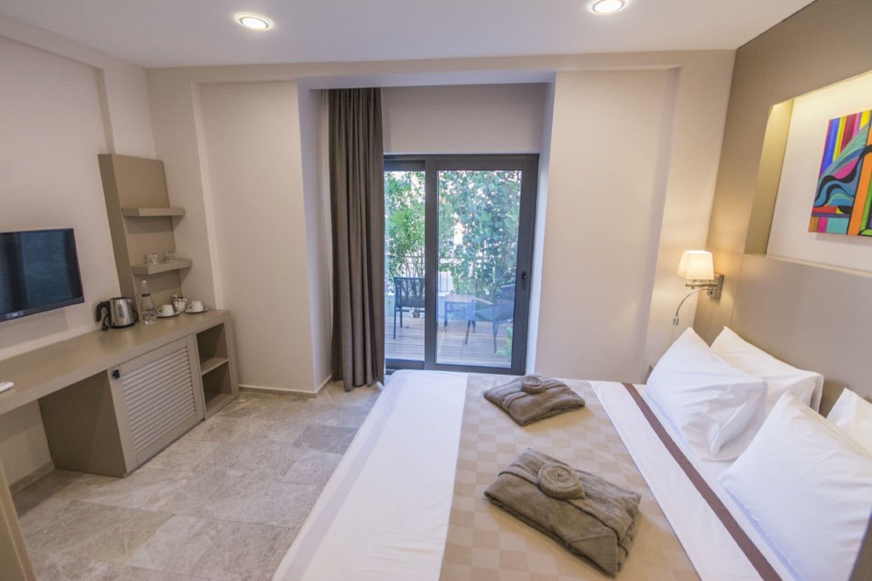 A hotel room with a bed, a desk with a television, a coffee maker, and a window with a view of the outdoors.