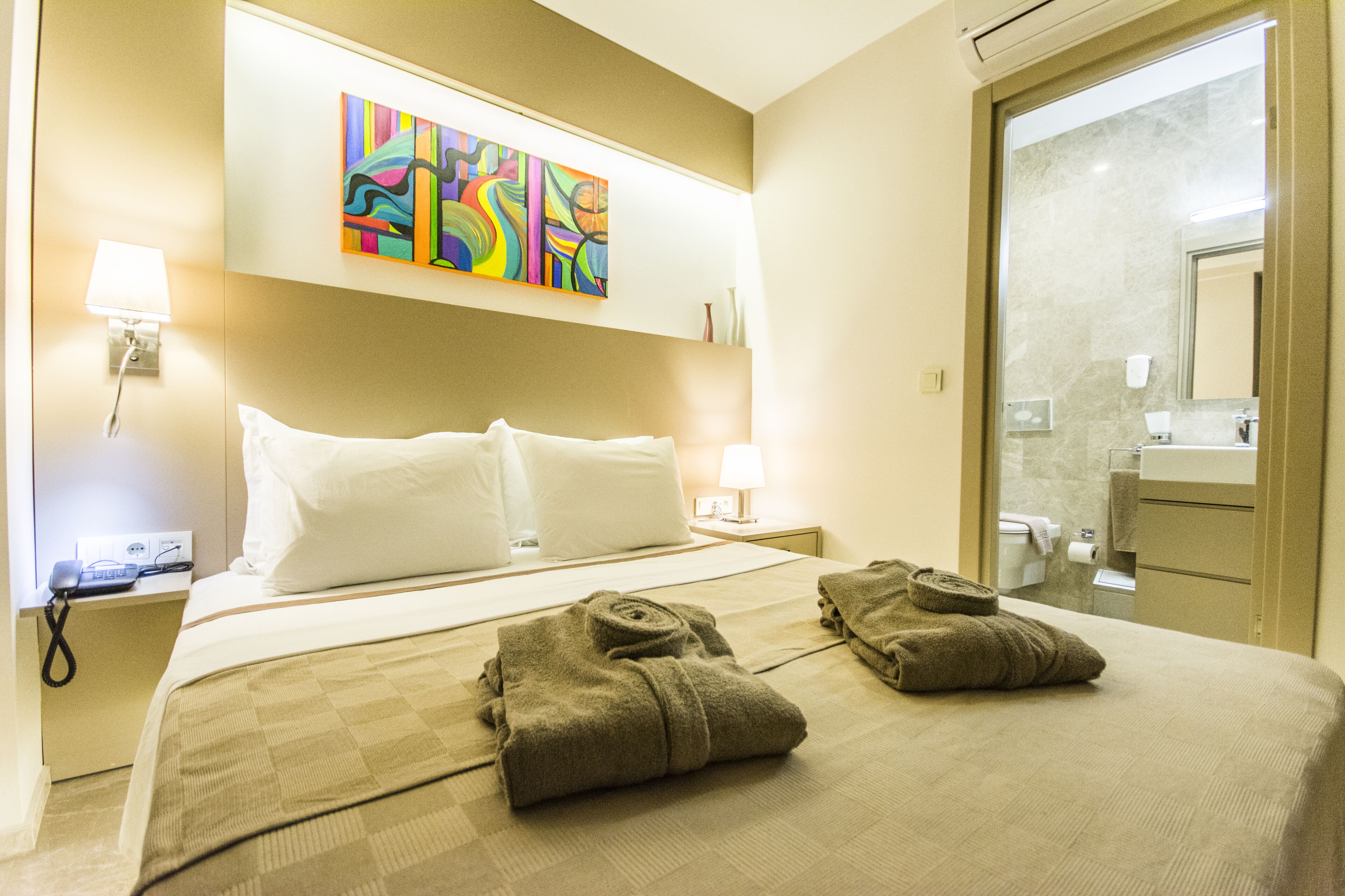 Ein Hotelzimmer mit einem Bett, zwei Handtüchern, einem Gemälde, einer Lampe und einem durchgegangenen Tür erkennbaren Badezimmer.