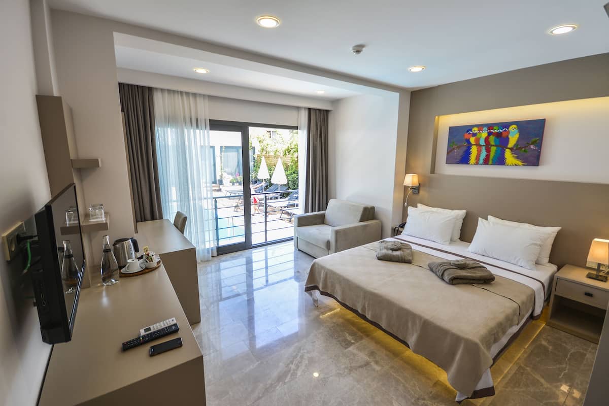 A hotel room with a bed, a desk with a TV, a chair, a nightstand, and a painting on the wall.