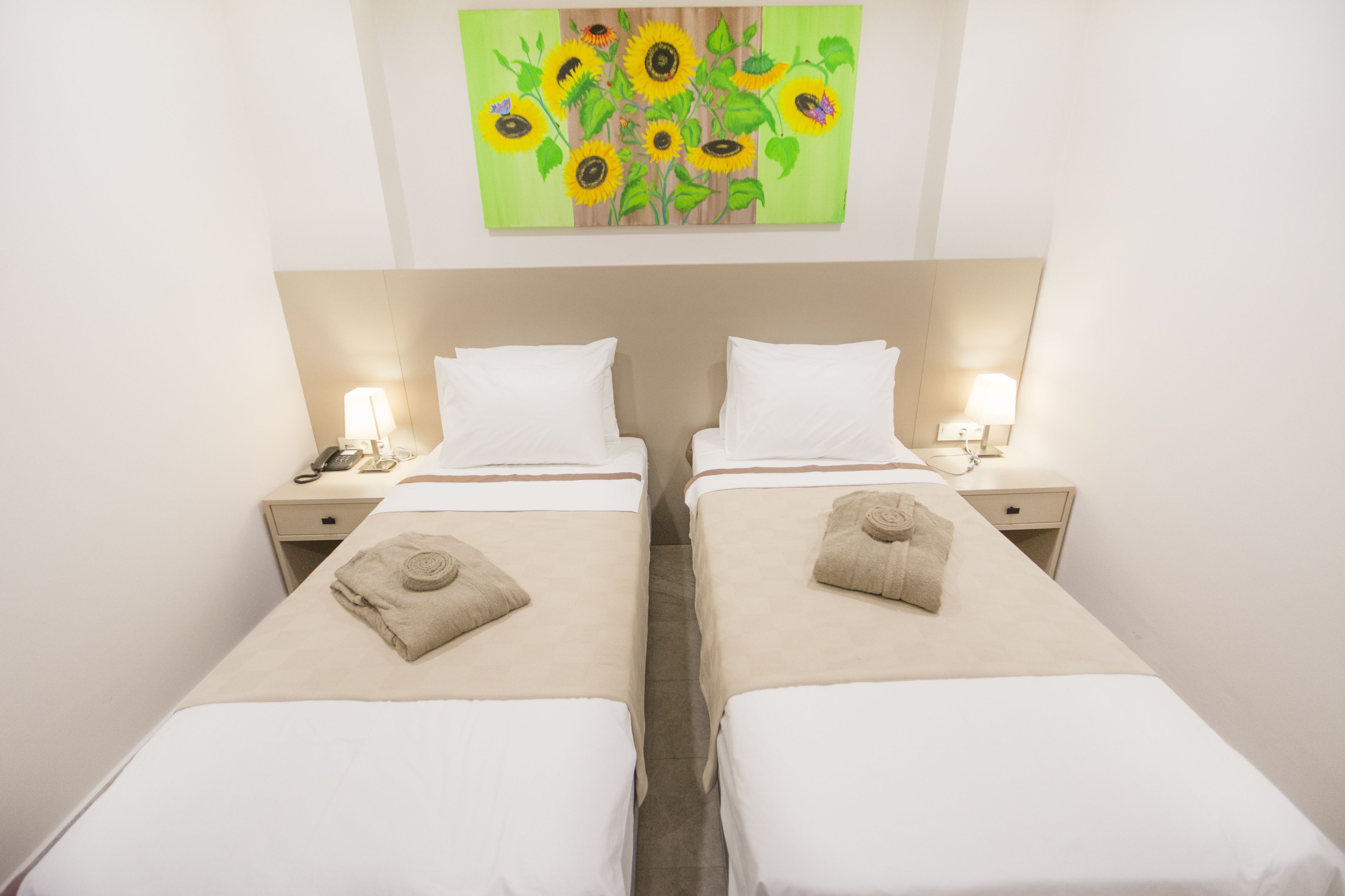 Een hotelkamer met twee bedden, elk voorzien van een kussen en een handdoek. Boven de bedden hangt een schilderij van zonnebloemen.