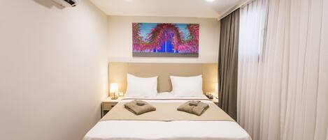 A hotel room with a bed, a nightstand, an air conditioner, a painting, and a window with curtains.