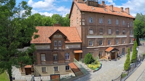 A multi-story hotel with a red-tiled roof, brick facade, and a small tower-like structure on the roof. - Hotel Młyn (Elblag)
