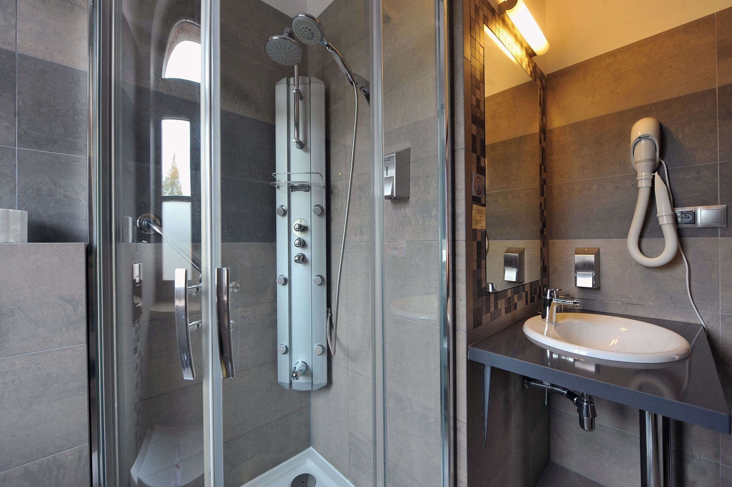 A modern bathroom with a glass-enclosed shower, a built-in sink, and a hairdryer mounted on the wall.