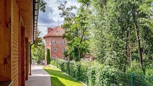 A pathway leading to a brick building with a red roof, surrounded by lush greenery and a green fence. - Hotel Młyn (Elblag)