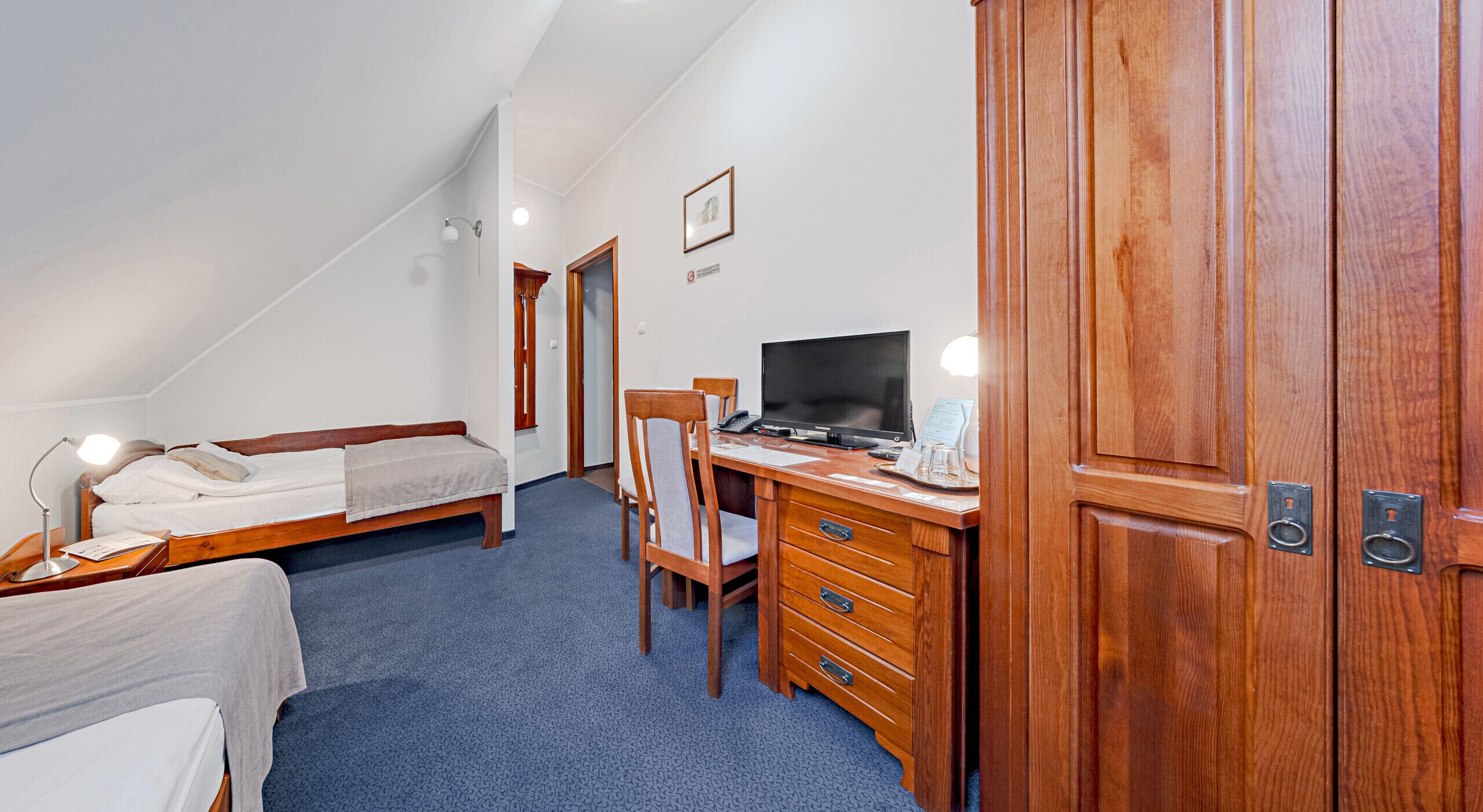 A hotel room with a bed, a desk with a computer, a chair, and a wardrobe.