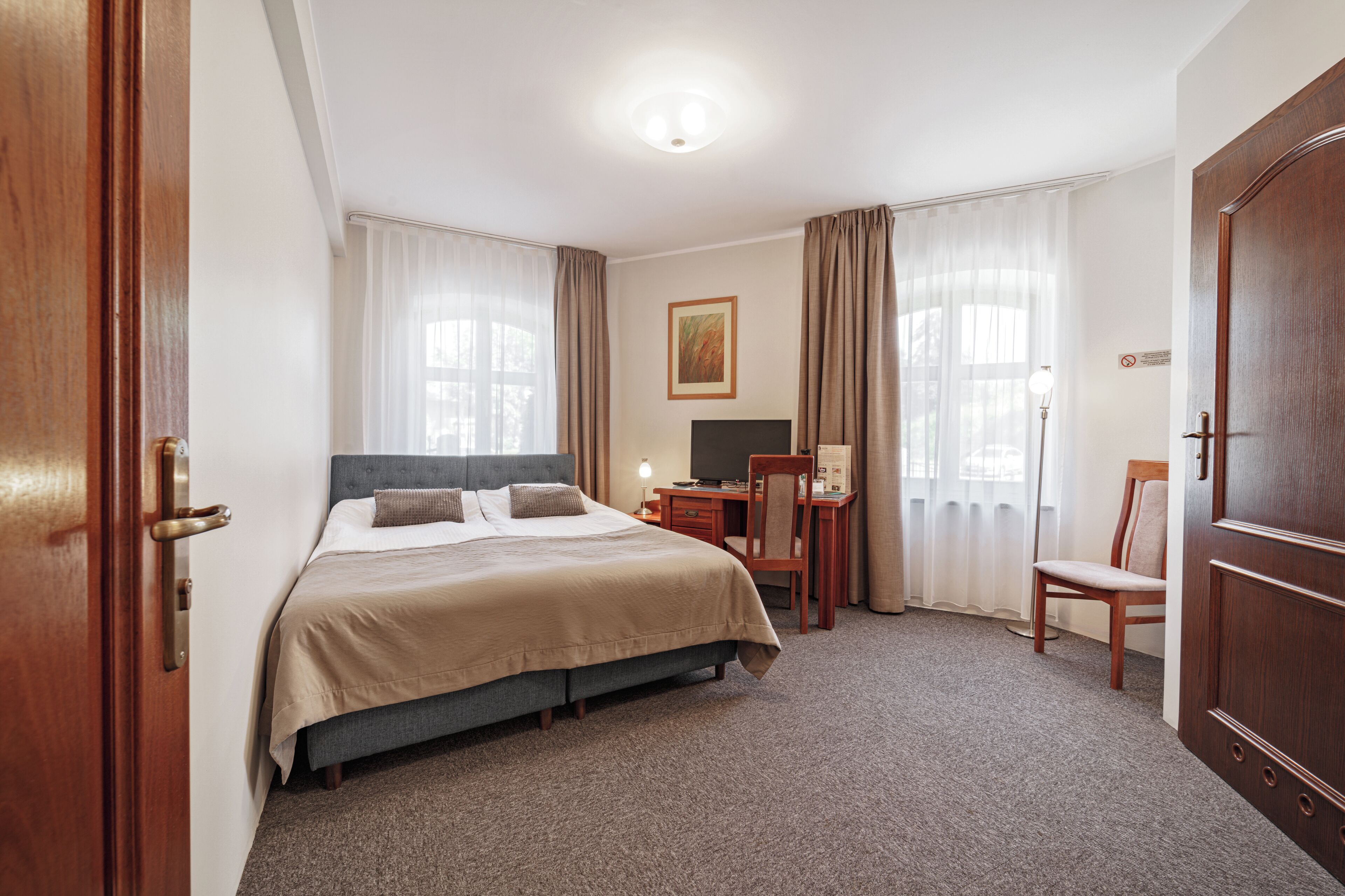A hotel room with a bed, desk, chair, and a television.