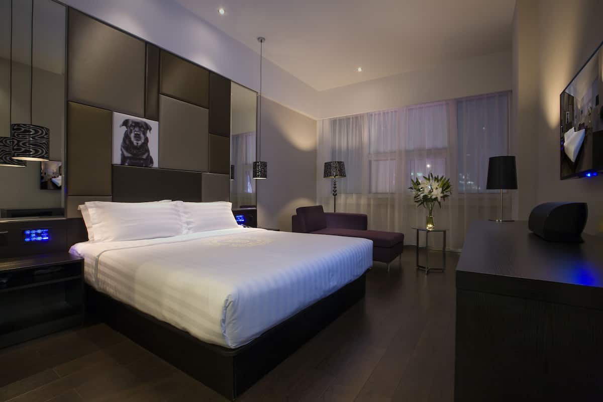 A modern hotel room with a large bed, a desk, a chair, a mirror, and a window with curtains.