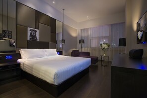 Una habitación de hotel moderna con una cama grande, un escritorio, una silla, un espejo y una ventana con cortinas.