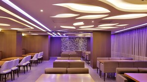 Un restaurante moderno con una barra alargada y cabinas, que presenta una pared con diseño y un techo con iluminación singular.