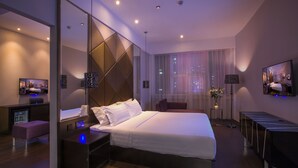 Una habitación de hotel moderna con una cama grande, mesitas de noche, un escritorio y una zona de estar.