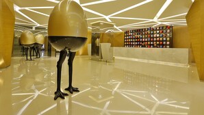 Un interior moderno con suelo reflectante, diseño geométrico en el techo y una pared llena de objetos esféricos de colores.