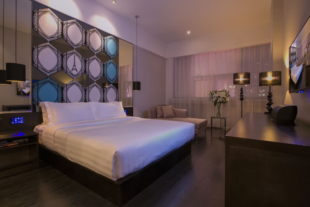 A modern hotel room with a large bed, a desk, a TV, and a decorative wall.