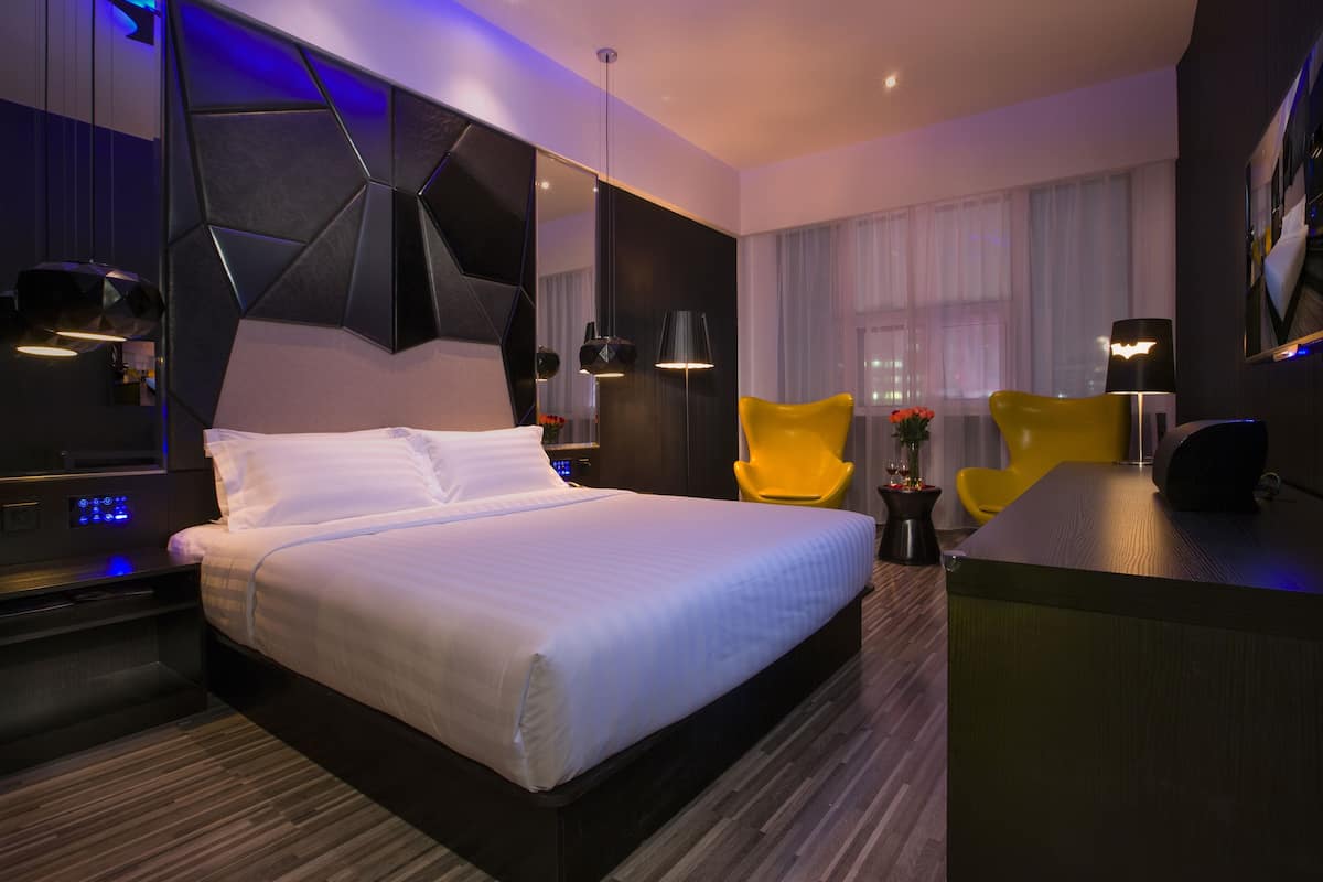 A modern hotel room with a large bed, a desk, a chair, and a mirror.
