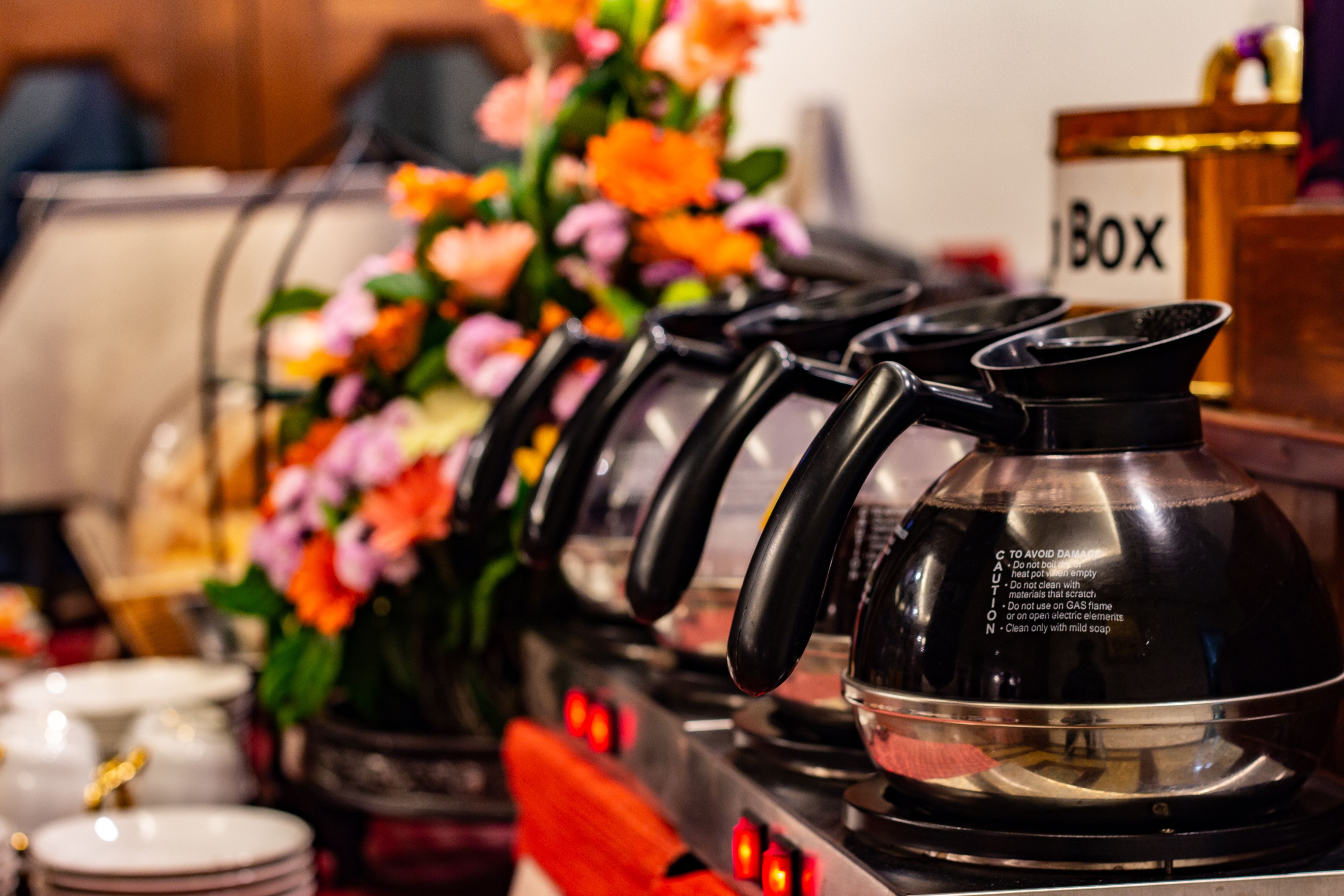 A coffee station with multiple kettles and a coffee pot, a flower arrangement, and a sign labeled "BOX".