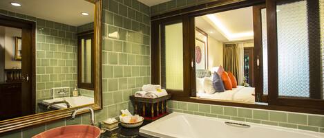 A bathroom with a large mirror, a white bathtub, a pink bowl sink, and a green tiled wall.