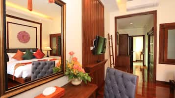 A hotel room with a bed, a large mirror, a television, a wooden desk, a chair, and a vase of flowers.