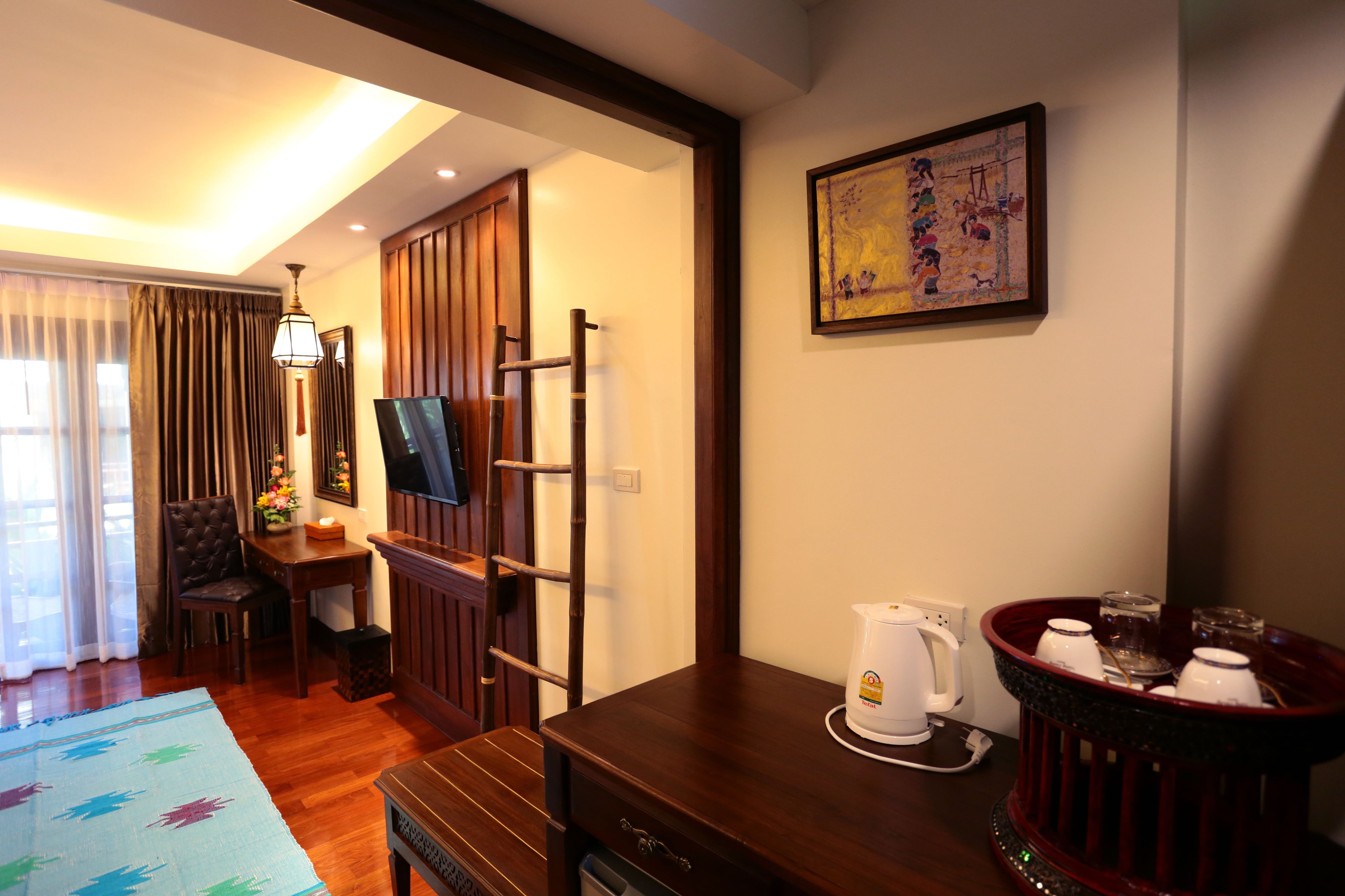 A hotel room with a wooden desk, a television, a coffee maker, and a tray with glasses and cups.